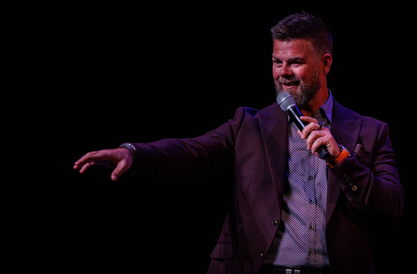 Adam Green on a dark stage, microphone in his right hand, his left arm reaching out to the audience.